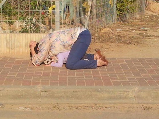 არეულობა ისრაელში. დედა გადაფარებულია შვილზე და იცავს მას საჰაერო დარტყმებისგან